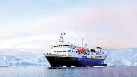 A ship sails through icy waters near icebergs - National Geographic Explorer, Lindblad Expeditions