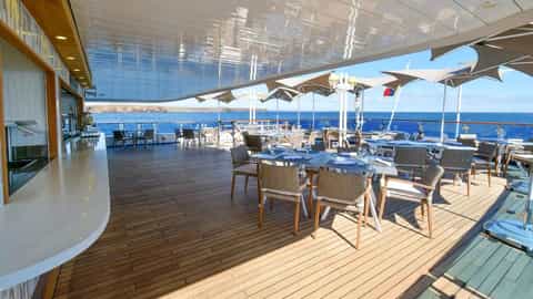 An outdoor dining area with tables, chairs, and a bar - National Geographic Gemini, Lindblad Expeditions