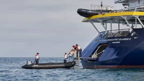 People board a ship from a small boat - National Geographic Islander 2, Lindblad Expeditions