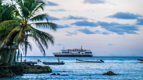 A ship sails on the ocean near a tropical shore - National Geographic Quest, Lindblad Expeditions