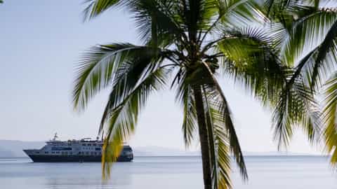 A ship sails on calm water near a tropical shore - National Geographic Quest, Lindblad Expeditions