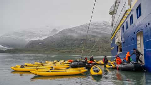 Kayaks and zodiacs are gathered near a blue cruise ship - National Geographic Resolution, Lindblad Expeditions
