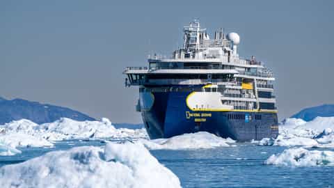 A ship sails through icebergs under a clear sky - National Geographic Resolution, Lindblad Expeditions