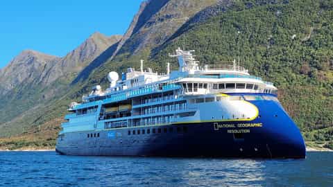 A cruise ship sails on the water near mountains - National Geographic Resolution, Lindblad Expeditions