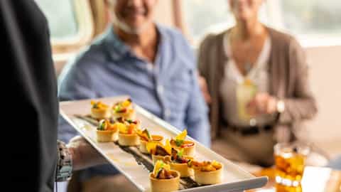 A waiter serves a tray of appetizers to a couple - National Geographic Sea Bird, Lindblad Expeditions