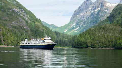 A ship sails through a narrow waterway between mountains - National Geographic Sea Bird, Lindblad Expeditions