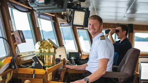 Captain smiles on the bridge while crew member uses binoculars - National Geographic Sea Bird, Lindblad Expeditions