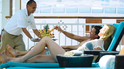 A server offers fruit skewers to a couple relaxing on lounge chairs - Norwegian Breakaway, Norwegian Cruise Line