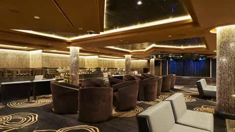 A lounge with plush seating and a stage area - Norwegian Gem, Norwegian Cruise Line