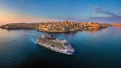 A cruise ship sails past a coastal city at sunset - Norwegian Viva, Norwegian Cruise Line