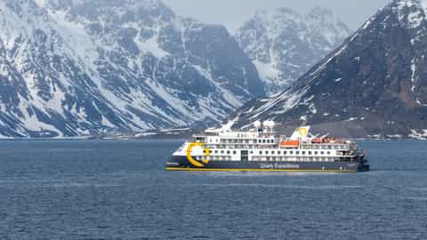 A ship sails in front of snow-covered mountains - Ocean Explorer, Quark Expeditions