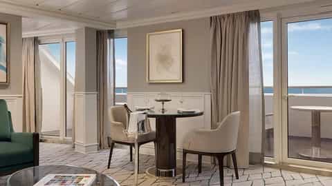 A suite living area with a dining table and balcony view - Oceania Sirena, Oceania Cruises