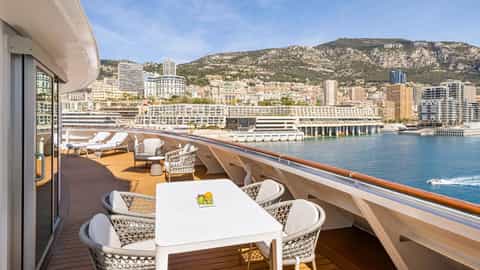 A balcony with a table, chairs, and lounge chairs - Oceania Vista, Oceania Cruises