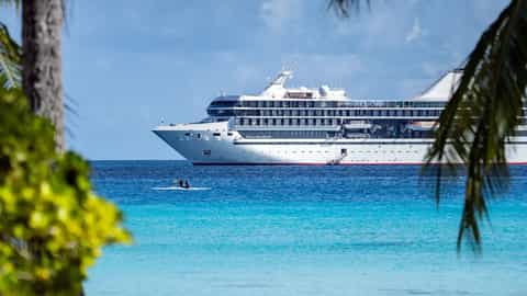 A large cruise ship sails on bright blue water - Paul Gauguin, Ponant Cruises