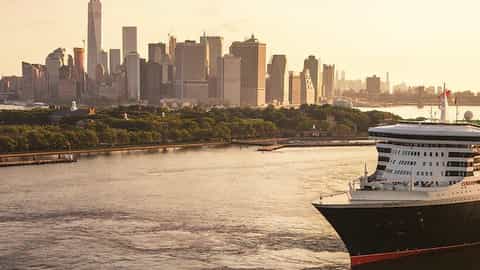 A large cruise ship sails past a city skyline - Queen Mary 2, Cunard