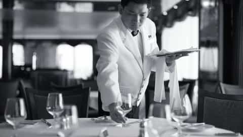 A waiter sets a table in a formal dining room - Queen Victoria, Cunard