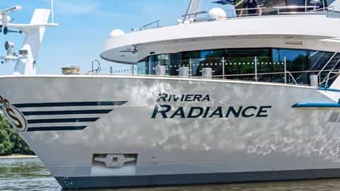 A white river cruise ship with blue trim sails on a river - Riviera Radiance, Riviera Travel