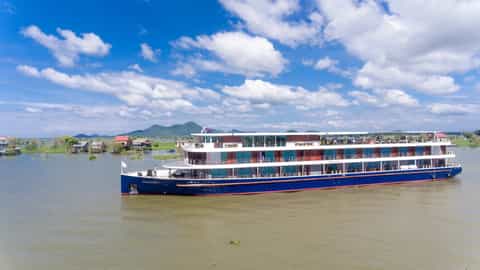 A blue and white river ship sails on a wide, calm river - RV Indochine II, CroisiEurope