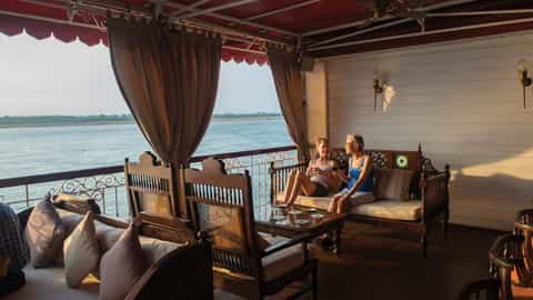 Two women relax on a covered balcony overlooking the water - RV Jahan, Lindblad Expeditions