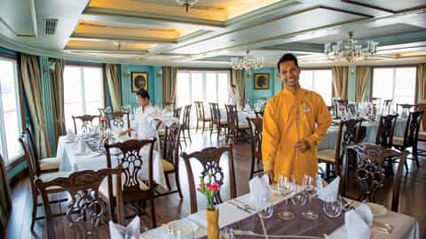 A waiter stands in a formal dining room with set tables - RV Jahan, Lindblad Expeditions