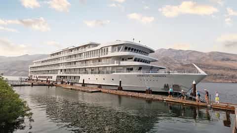 A large white cruise ship is docked at a pier - ACL American Harmony, American Cruise Lines