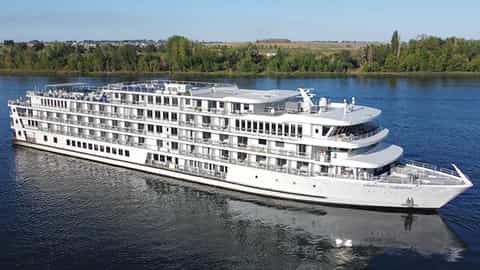 A white river cruise ship sails on a blue river - ACL American Harmony, American Cruise Lines