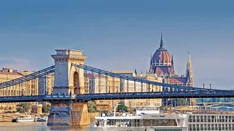 A river ship sails past a bridge and city buildings - Scenic Ruby, Scenic Cruises