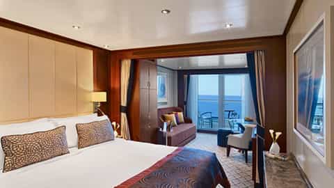 A suite with a bed, seating area, and balcony overlooking the ocean - Seabourn Encore, Seabourn Cruises