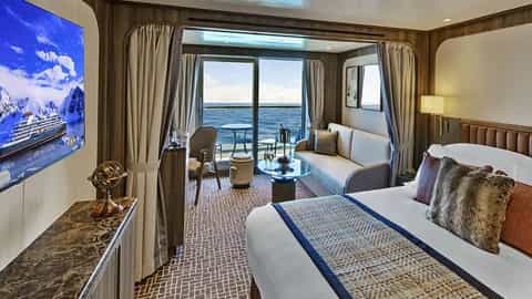 A suite with a bed, sofa, and balcony overlooking the ocean - Seabourn Venture, Seabourn Cruises