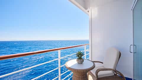 A private balcony with chairs and a table overlooks the ocean - Seven Seas Voyager, Regent Seven Seas Cruises