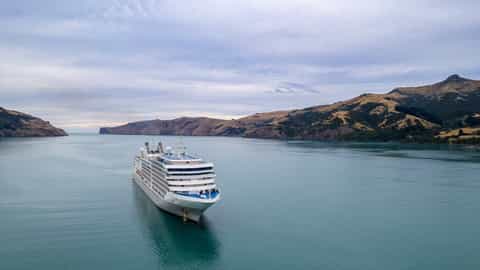 A large cruise ship sails on calm water near a mountainous coastline - Silver Muse, Silversea Cruises