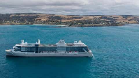 A large cruise ship sails on the blue ocean near a coastline - Silver Nova, Silversea Cruises