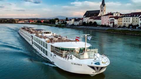 A river cruise ship sails past a European town at dusk - SS Beatrice, Ponant Cruises
