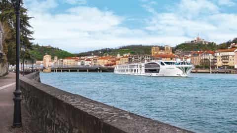 A river ship sails past a European city on a sunny day - SS Catherine, Uniworld