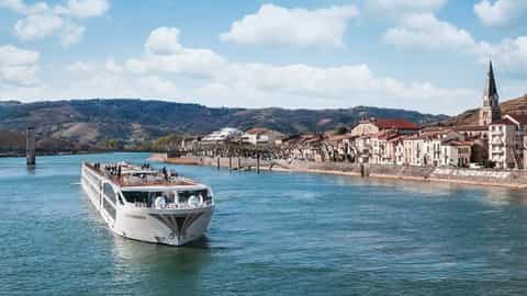 A riverboat sails past a town on the riverbank - SS Catherine, Uniworld