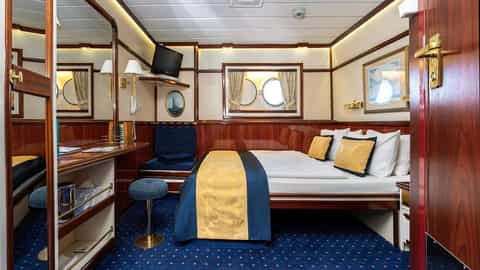 A ship cabin with a bed, desk, and porthole window - Star Flyer, Star Clippers
