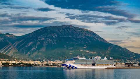 A large cruise ship is docked near a coastal town and mountain - Star Princess, Princess Cruises