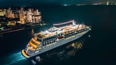 A cruise ship sails at night near a lit-up coastline - Star Seeker, Windstar Cruises